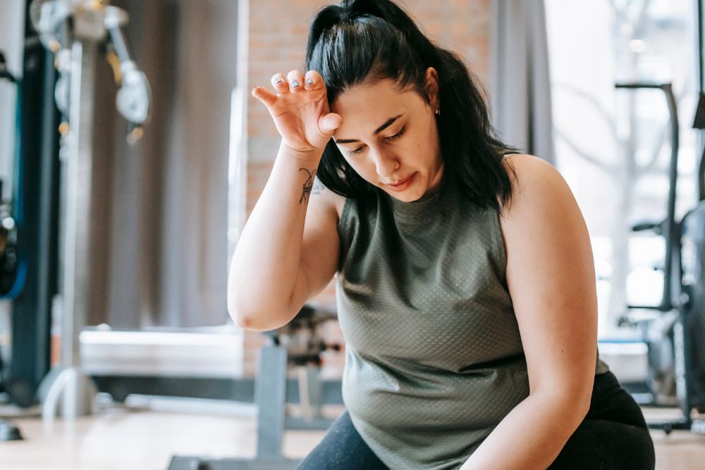 Fatigued woman wiping sweat during a workout, highlighting how low energy and iron deficiency affect stamina.