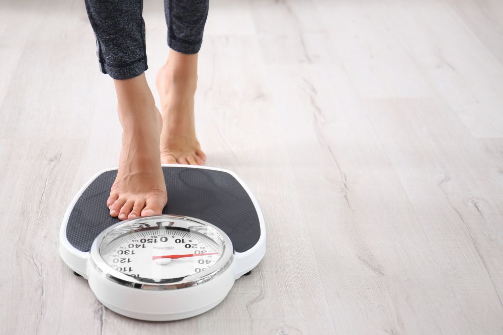 A person stepping onto a scale, indicating a focus on weight management and health monitoring, possibly linked to conditions like anemia or low iron levels.